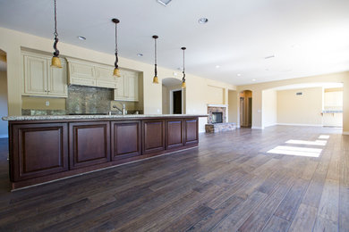 Photo of an expansive traditional l-shaped eat-in kitchen in Orange County with medium hardwood floors, a double-bowl sink, recessed-panel cabinets, beige cabinets, granite benchtops, beige splashback, stone slab splashback, stainless steel appliances, with island, brown floor and beige benchtop.