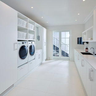 Photo of a modern galley utility room in London with a single-bowl sink, white walls, ceramic flooring, a side by side washer and dryer, flat-panel cabinets, white cabinets and composite countertops.