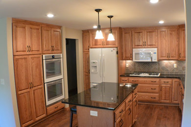 Traditional u-shaped eat-in kitchen in Minneapolis with an undermount sink, raised-panel cabinets, medium wood cabinets, granite benchtops, multi-coloured splashback, ceramic splashback and white appliances.