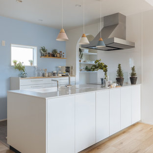 This is an example of a mid-sized scandinavian single-wall open plan kitchen in Other with flat-panel cabinets, white cabinets, white splashback, light hardwood floors, beige floor, white benchtop and wallpaper.