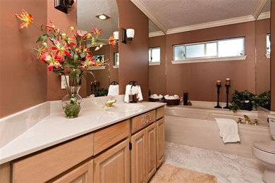 Pebble tile floor alcove bathtub photo in Vancouver with an integrated sink, raised-panel cabinets, light wood cabinets, solid surface countertops, a one-piece toilet and brown walls