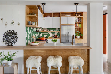 Design ideas for a modern u-shaped kitchen in New York with a farmhouse sink, flat-panel cabinets, white cabinets, wood benchtops, green splashback, cement tile splashback, stainless steel appliances, light hardwood floors and no island.