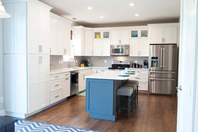 Inspiration for a mid-sized transitional l-shaped medium tone wood floor and brown floor eat-in kitchen remodel in Other with an undermount sink, shaker cabinets, white cabinets, quartz countertops, gray backsplash, mosaic tile backsplash, stainless steel appliances, an island and white countertops