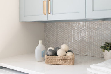 Example of a mid-sized beach style galley ceramic tile and beige floor dedicated laundry room design in DC Metro with an undermount sink, shaker cabinets, blue cabinets, quartz countertops, white backsplash, mosaic tile backsplash, white walls, a side-by-side washer/dryer and white countertops