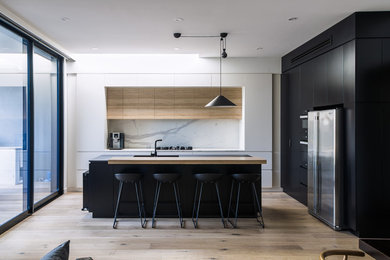 Mid-sized modern u-shaped eat-in kitchen in Melbourne with flat-panel cabinets, stone slab splashback, with island, a single-bowl sink, stainless steel appliances and light hardwood floors.