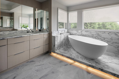 Inspiration for a large contemporary master multicolored tile marble floor, multicolored floor and double-sink freestanding bathtub remodel in New York with flat-panel cabinets, light wood cabinets, gray walls, an undermount sink, marble countertops, multicolored countertops and a built-in vanity