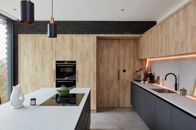 Design ideas for a large contemporary l-shaped open plan kitchen in London with an undermount sink, flat-panel cabinets, light wood cabinets, quartz benchtops, white splashback, engineered quartz splashback, stainless steel appliances, limestone floors, with island, grey floor and white benchtop.