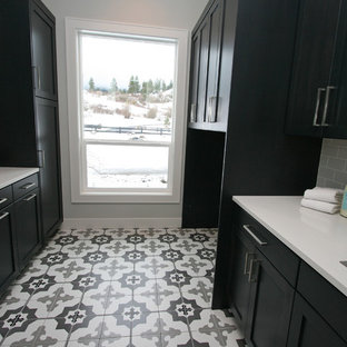 Foto de cuarto de lavado de galera, contemporáneo, de tamaño medio, con fregadero bajoencimera, armarios estilo shaker, puertas de armario negras, encimera de cuarzo compacto, paredes grises, suelo de baldosas de cerámica, lavadora y secadora juntas, suelo multicolor y encimeras blancas