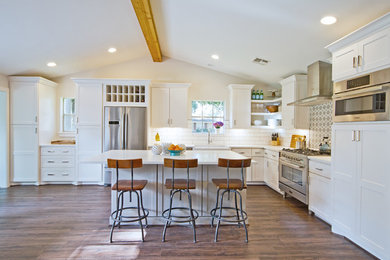 Inspiration for a transitional open plan kitchen in Houston with a farmhouse sink, shaker cabinets, white cabinets, quartz benchtops, white splashback, ceramic splashback, stainless steel appliances, vinyl floors, with island, brown floor and white benchtop.