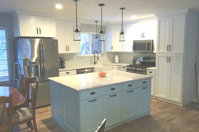 This is an example of a large modern l-shaped kitchen pantry in Salt Lake City with with island, a farmhouse sink, recessed-panel cabinets, white cabinets, quartz benchtops, stainless steel appliances, light hardwood floors, white splashback, mosaic tile splashback, beige floor and white benchtop.