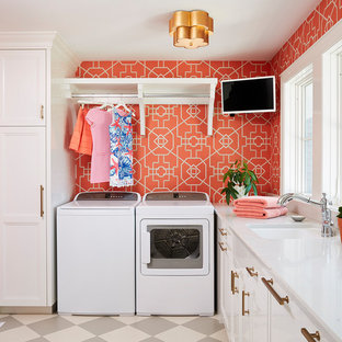 Modelo de cuarto de lavado clásico con fregadero bajoencimera, armarios con paneles empotrados, puertas de armario blancas, lavadora y secadora juntas, suelo multicolor, encimeras blancas y paredes rojas