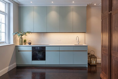 Foto på ett litet funkis linjärt kök med öppen planlösning, med en nedsänkt diskho, släta luckor, blå skåp, marmorbänkskiva, vitt stänkskydd, svarta vitvaror, mörkt trägolv och svart golv