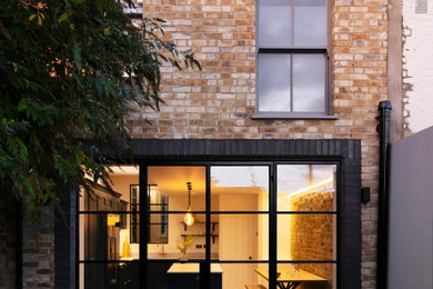 Medium sized contemporary brick and rear house exterior in London with three floors, a pitched roof, a tiled roof and a black roof.