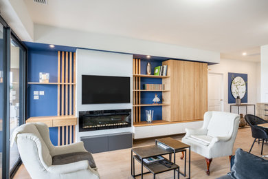 Aménagement d'un salon blanc et bois éclectique de taille moyenne avec un mur bleu, parquet clair, une cheminée standard, un manteau de cheminée en plâtre et un téléviseur fixé au mur.