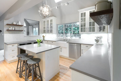 Arts and crafts u-shaped light wood floor kitchen photo in Vancouver with a farmhouse sink, shaker cabinets, white cabinets, quartz countertops, white backsplash, subway tile backsplash, stainless steel appliances and an island