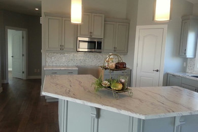 Eat-in kitchen - mid-sized transitional l-shaped vinyl floor eat-in kitchen idea in Calgary with raised-panel cabinets, gray cabinets, laminate countertops, stainless steel appliances, an island, a drop-in sink, gray backsplash and ceramic backsplash