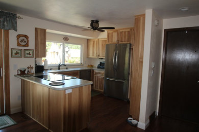 Example of a small mountain style u-shaped dark wood floor eat-in kitchen design in Denver with an integrated sink, raised-panel cabinets, light wood cabinets, solid surface countertops, stainless steel appliances and a peninsula