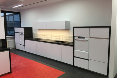 Photo of an expansive contemporary galley separate kitchen in Leipzig with a drop-in sink, flat-panel cabinets, white cabinets, wood benchtops, white splashback, ceramic splashback, stainless steel appliances, linoleum floors, no island, red floor and black benchtop.