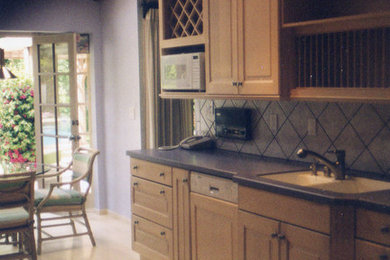 Example of a mid-sized classic galley light wood floor eat-in kitchen design in Orange County with an integrated sink, raised-panel cabinets, light wood cabinets, solid surface countertops, beige backsplash, ceramic backsplash, stainless steel appliances and no island