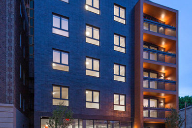 Large contemporary brick grey apartment exterior in New York with a flat roof and a tile roof.