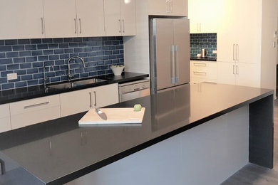 Photo of a large modern galley kitchen pantry in Brisbane with a double-bowl sink, flat-panel cabinets, white cabinets, quartz benchtops, blue splashback, subway tile splashback, stainless steel appliances, with island and black benchtop.