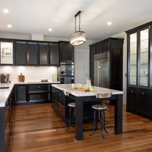 This is an example of an expansive transitional u-shaped kitchen in Other with an undermount sink, recessed-panel cabinets, black cabinets, window splashback, with island, brown floor and white benchtop.
