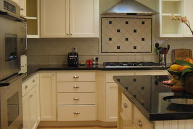 Mid-sized elegant l-shaped light wood floor and brown floor enclosed kitchen photo in San Francisco with black backsplash, shaker cabinets, white cabinets, stainless steel appliances, an island, an undermount sink, granite countertops and ceramic backsplash