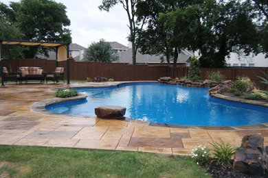 Example of a large transitional backyard custom-shaped and stamped concrete pool fountain design in Dallas