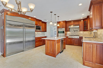 Example of a mid-sized classic l-shaped beige floor and travertine floor kitchen design in New Orleans with raised-panel cabinets, medium tone wood cabinets, granite countertops, multicolored backsplash, matchstick tile backsplash, stainless steel appliances, an island and a double-bowl sink