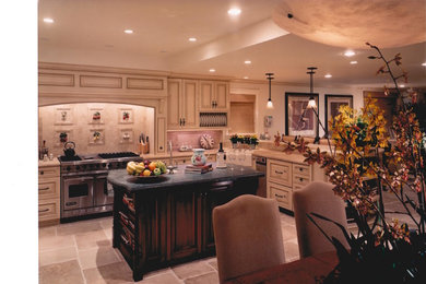 Inspiration for a mid-sized timeless u-shaped limestone floor open concept kitchen remodel in Orange County with a farmhouse sink, raised-panel cabinets, beige cabinets, limestone countertops, beige backsplash, stone tile backsplash, stainless steel appliances and an island