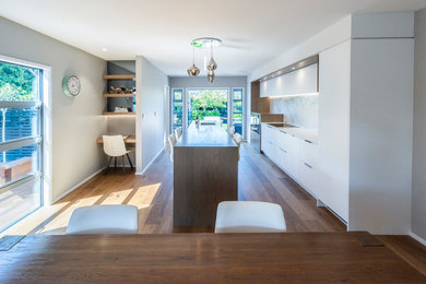 Mid-sized contemporary galley eat-in kitchen in Christchurch with white splashback, marble splashback, light hardwood floors, with island, brown floor and white benchtop.