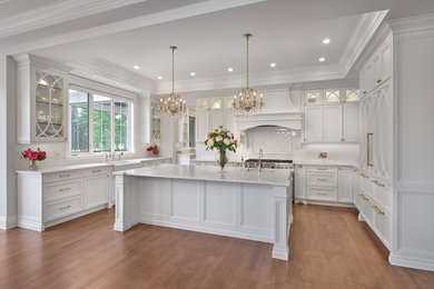 Inspiration for a large classic u-shaped kitchen/diner in Edmonton with a belfast sink, recessed-panel cabinets, white cabinets, engineered stone countertops, white splashback, ceramic splashback, integrated appliances, medium hardwood flooring, an island, brown floors, white worktops and a drop ceiling.