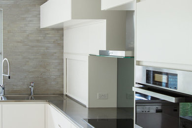 Modern kitchen in Sydney with with island, flat-panel cabinets, white cabinets, stainless steel benchtops, grey splashback, glass tile splashback, a double-bowl sink and limestone floors.