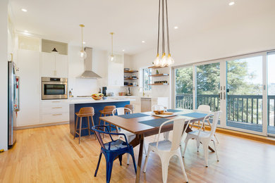 Inspiration for a mid-sized modern eat-in kitchen in San Francisco with a farmhouse sink, flat-panel cabinets, white cabinets, white splashback, ceramic splashback, stainless steel appliances, light hardwood floors and with island.