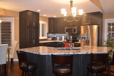 Large l-shaped dark wood floor kitchen photo in Calgary with a double-bowl sink, raised-panel cabinets, dark wood cabinets, granite countertops, stainless steel appliances and an island