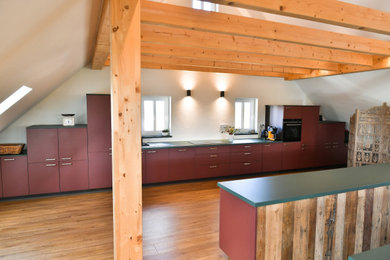 Zweizeilige, Große Moderne Küche mit integriertem Waschbecken, flächenbündigen Schrankfronten, roten Schränken, Mineralwerkstoff-Arbeitsplatte, Küchenrückwand in Weiß, schwarzen Elektrogeräten, zwei Kücheninseln, braunem Boden, grüner Arbeitsplatte und freigelegten Dachbalken in Nürnberg