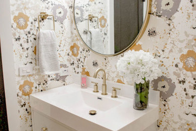 Example of a mid-sized transitional white tile and porcelain tile medium tone wood floor, brown floor and wallpaper powder room design in Chicago with shaker cabinets, white cabinets, a one-piece toilet, multicolored walls, an integrated sink, white countertops and a built-in vanity