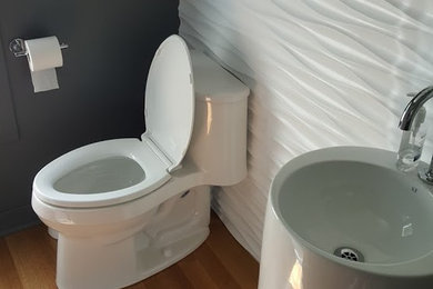 Modelo de cuarto de baño minimalista de tamaño medio con sanitario de una pieza, suelo de madera clara, aseo y ducha y lavabo con pedestal