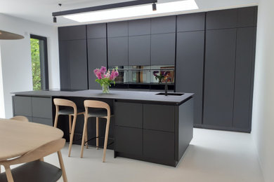 バッキンガムシャーにある高級な中くらいなコンテンポラリースタイルのおしゃれなキッチン (フラットパネル扉のキャビネット、黒いキャビネット、黒い調理設備、黒いキッチンカウンター) の写真