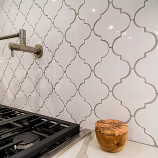 Inredning av ett klassiskt vit vitt skafferi, med vita skåp, bänkskiva i kvarts, orange stänkskydd, stänkskydd i porslinskakel, rostfria vitvaror, mellanmörkt trägolv, en köksö och brunt golv