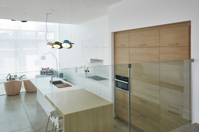 Design ideas for a modern galley open plan kitchen with a submerged sink, flat-panel cabinets, white cabinets, engineered stone countertops, white splashback, engineered quartz splashback, integrated appliances, concrete flooring, an island, grey floors and white worktops.