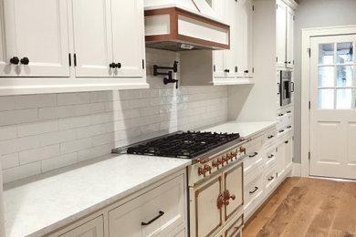 Inspiration for a large cottage l-shaped medium tone wood floor, multicolored floor and exposed beam eat-in kitchen remodel with a farmhouse sink, recessed-panel cabinets, white cabinets, quartz countertops, white backsplash, subway tile backsplash, paneled appliances, an island and white countertops