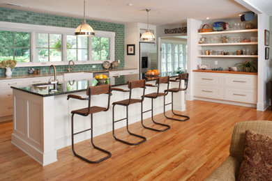 Example of a large transitional medium tone wood floor and brown floor open concept kitchen design in Other with a farmhouse sink, shaker cabinets, white cabinets, green backsplash, subway tile backsplash, stainless steel appliances and an island