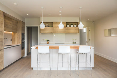 Photo of a mid-sized contemporary galley open plan kitchen in Dublin with a single-bowl sink, flat-panel cabinets, light wood cabinets, quartzite benchtops, white splashback, stone slab splashback, stainless steel appliances, light hardwood floors and with island.
