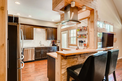 Open concept kitchen - mid-sized contemporary l-shaped medium tone wood floor and brown floor open concept kitchen idea in Denver with a drop-in sink, raised-panel cabinets, brown cabinets, wood countertops, white backsplash, subway tile backsplash, stainless steel appliances, a peninsula and beige countertops