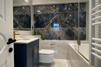 Photo of a medium sized modern bathroom in London with shaker cabinets, blue cabinets, a built-in bath, an alcove shower, a wall mounted toilet, blue tiles, porcelain tiles, white walls, porcelain flooring, an integrated sink, quartz worktops, white floors, an open shower, white worktops, a feature wall, a single sink and a freestanding vanity unit.