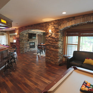 Large rustic basement in Milwaukee with beige walls, dark hardwood flooring, a two-sided fireplace and a stone fireplace surround.