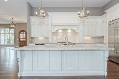 Example of a large transitional l-shaped medium tone wood floor and brown floor open concept kitchen design in St Louis with shaker cabinets, white cabinets, marble countertops, white backsplash, subway tile backsplash, stainless steel appliances, an island and a farmhouse sink
