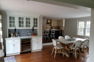 Inspiration for a small transitional single-wall medium tone wood floor and brown floor wet bar remodel in New York with no sink, glass-front cabinets, white cabinets, quartz countertops, multicolored backsplash and white countertops