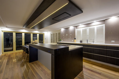 Inspiration for a large contemporary l-shaped eat-in kitchen in Newcastle - Maitland with a double-bowl sink, flat-panel cabinets, dark wood cabinets, quartz benchtops, beige splashback, black appliances, light hardwood floors, with island and brown floor.